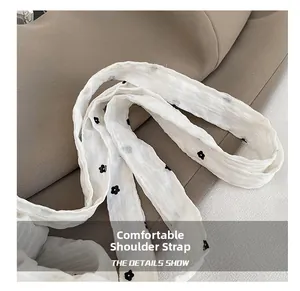 Détail de la bandoulière en tissu blanc avec motif floral noir et texture plissée