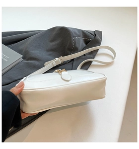 Dettaglio della base larga e della fibbia dorata di una borsa a tracolla bianco crema
