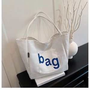 Close-up of a white canvas tote bag with blue bag print and fashion label on a shelf