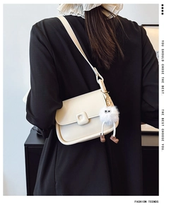 Close-up of a cream crossbody bag with a square buckle and a cute plush monster charm