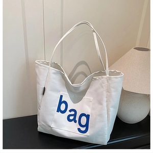 Detail of white canvas tote bag with front pocket and blue letter print in a home setting