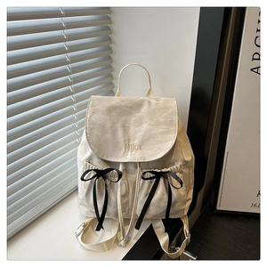 Détail d'un sac à dos plissé beige clair avec broderie Nika et nœuds noirs