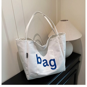 Detail of white canvas tote bag featuring a blue 'bag' print and a small fashion tag