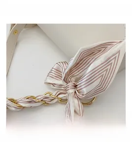 Detail of white leather bag with gold chain strap and striped silk bow decoration