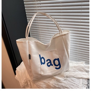 Detail of white canvas tote bag with blue bag print and side fashion label on lace cloth