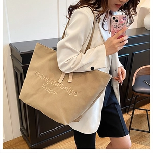 Canvas tote bag worn over shoulder showing khaki fabric texture and letter embroidery