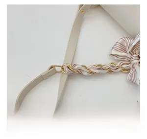 Detail of beige shoulder strap with interwoven pink scarf and gold chain accents