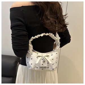 Detail of white pleated handbag with bow accents and heart pendant on shoulder