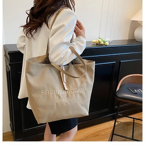 Detail of a large beige canvas tote bag showing the textured fabric and shoulder strap