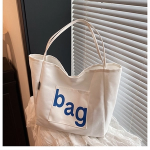 Close-up of white canvas tote bag with blue bag text on soft fabric background