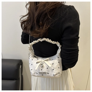 Detail of white pleated handbag featuring black bow prints and metal heart pendant