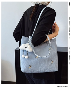 Detail of light blue tote bag with woven handles, gold butterflies and plush cloud charm