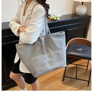 Detail of grey canvas tote bag with white letter embroidery and long shoulder strap