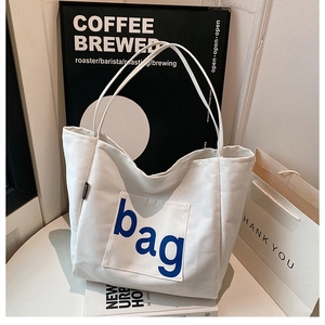 Detail of canvas tote bag featuring an outer pocket with a large blue bag lettering print