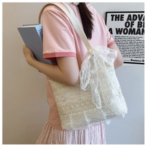 Detail view of white lace tote bag featuring a decorative large bow and leather strap