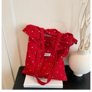 Detail of red floral tote bag with frilled edges on a book and artistic vase background