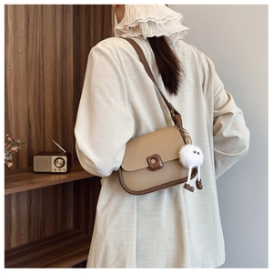 Detail of khaki shoulder bag with dark brown trim and a white plush monster charm