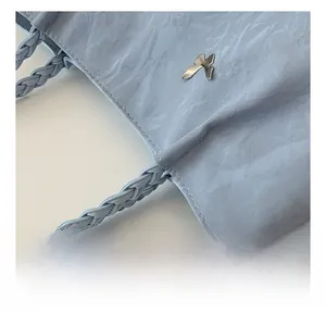 Detail of light blue tote bag with silver bird logo and braided handle craft
