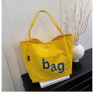 Detail of yellow canvas tote bag with bag embroidery placed on books in a stylish setting