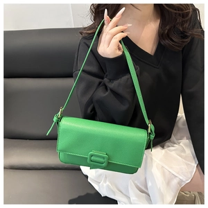 Close-up of green pebble grain leather baguette bag with gold hardware on black sofa