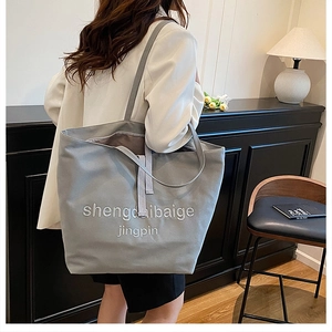 Détail du grand sac cabas en toile grise avec lettrage brodé sur le côté du sac à main