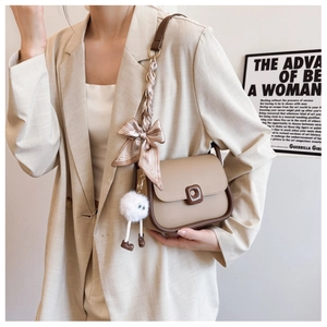 Detail of beige flap bag with silk scarf on strap and cute plush doll pendant accessory