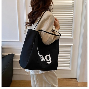 Detail of black canvas tote bag with white AG letters and slim shoulder straps
