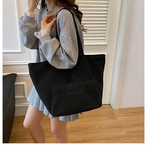 Detail of black canvas tote bag featuring embossed lettering and long shoulder straps
