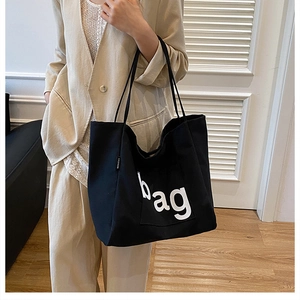 Close-up of black canvas tote bag showing white BAG print and FASHION side label