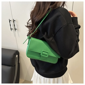 Close-up of green lychee leather baguette bag with minimalist rectangular buckle and strap