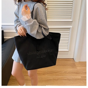 Detailed close-up of large black canvas tote bag with embossed text worn by a model