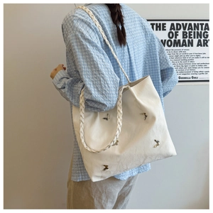Detail of white tote bag with silver metal butterflies and woven strap on model