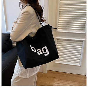 Detail of a black canvas tote bag with white bag lettering worn by a model in a suit