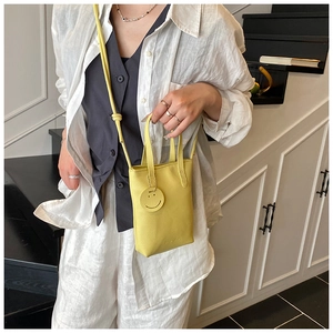 Detail of a bright yellow textured leather mini bag with cute smiley charm and strap