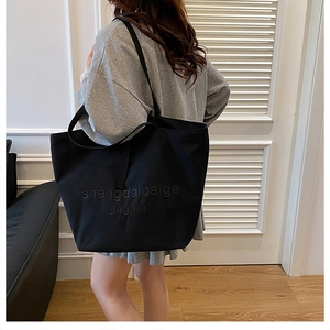 Black canvas tote bag shown on model's shoulder to display large capacity and style