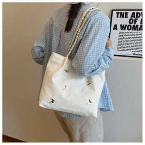 Detail of white tote bag with silver butterfly charms and woven rope shoulder strap
