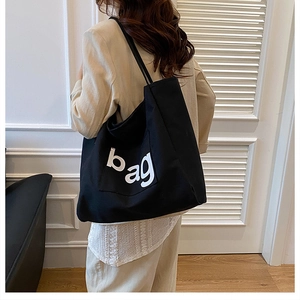 Detail view of large black canvas tote bag with white BAG text print on a model