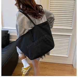 Large black canvas tote bag with embossed text shown on a model in a cozy home setting