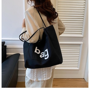 Close-up of a large black canvas tote bag with white bag lettering on a model