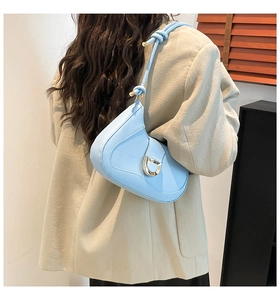 Detail of light blue saddle bag on beige blazer showing horseshoe buckle and knotted strap