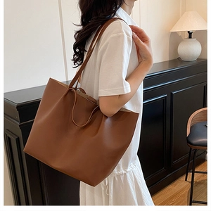 Side view of a large brown faux leather tote bag worn by a model in a minimalist setting