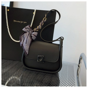 Detail of black crossbody bag with bold piping and chic black and white striped bow