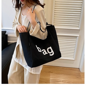 Detail of a black canvas tote bag showing the side pocket and white printed 'bag' lettering