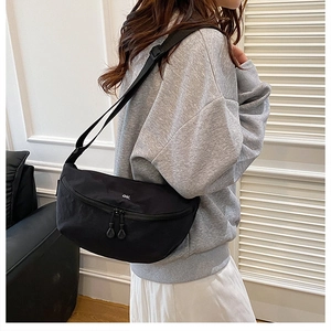 Side view of black crescent crossbody bag with white ok logo on casual urban outfit