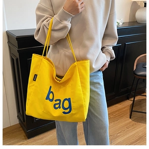 Detail of yellow canvas tote bag featuring large blue lettering and black fashion label