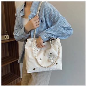 White textured tote bag featuring a metallic butterfly charm and woven shoulder strap