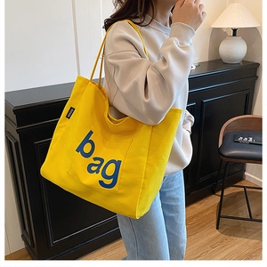 Detail of yellow canvas tote bag featuring blue bag lettering and fashion side label