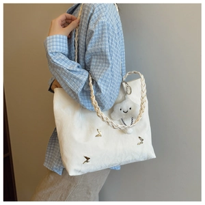 White large tote bag detail with silver butterflies and braided strap on model