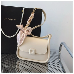 Detail of cream square crossbody bag with silk scarf wrapped chain strap and flip cover