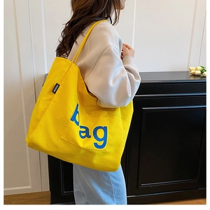 Close-up of yellow canvas tote bag with blue bag lettering and side pocket